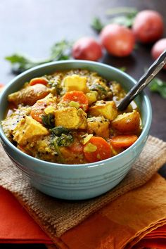 a blue bowl filled with vegetable stew on top of a napkin next to tomatoes and parsley