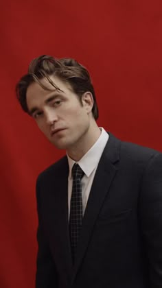 a man in a suit and tie standing against a red background