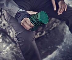 a man holding a green coffee cup in his left hand while sitting on a rock