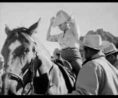 black and white photograph of people riding horses with hats on their heads, one man is holding the horse's bridle