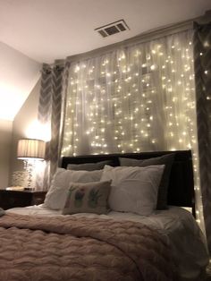 a bed that has some lights on the headboard and curtains over it in front of a window