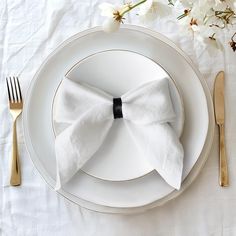 a white plate topped with a bow napkin and silverware next to a flower bouquet