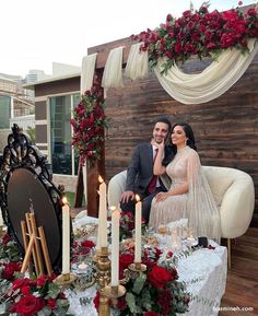 a man and woman sitting on a couch in front of a table covered with candles