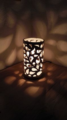 a lit candle sitting on top of a wooden table next to a shadow cast wall