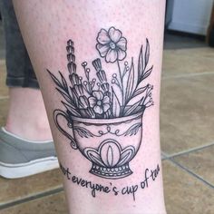 a tattoo on the leg of a woman with flowers in a cup and words written below it