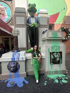 a woman in green pants standing next to a statue of a frog on top of a castle