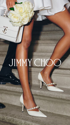 a woman in white high heels holding a bouquet of flowers and a purse with the words jimmy choo on it