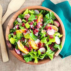 a wooden bowl filled with salad next to a green napkin and two wooden spoons