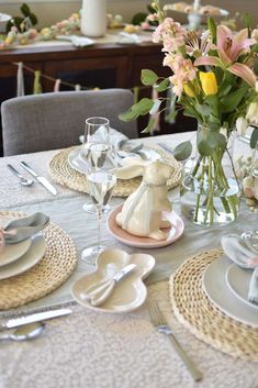 a table set with place settings and flowers in vases on the centerpiece, along with silverware