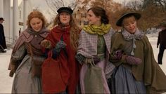 four women dressed in period clothing walking through the snow with one holding her hand on her hip