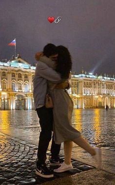 two people hugging each other in front of a building with a red heart flying overhead