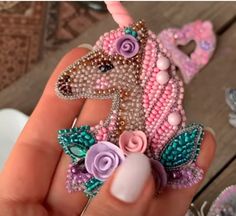 a hand holding a pink and purple pony brooch on it's finger,