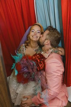 a man and woman are kissing in front of red curtained drapes with feathers on them