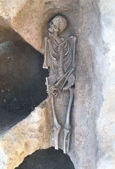 a skeleton sitting on top of a rock next to a hole in the ground that has been carved into it