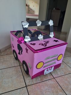 a pink cardboard box shaped like a car with flowers on the front and side, sitting on tile flooring