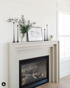 a white fireplace with some plants on top and pictures above the fire place in front of it