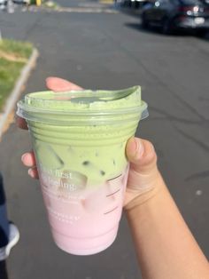 a hand holding up a green drink in a cup on the side of the road