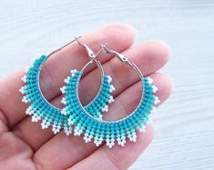 a hand holding a pair of blue and white beaded hoop earrings