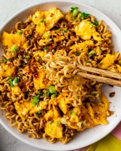 a white bowl filled with noodles and vegetables next to chopsticks on a table