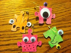 four pieces of paper with googly eyes hanging from strings on a wooden table top