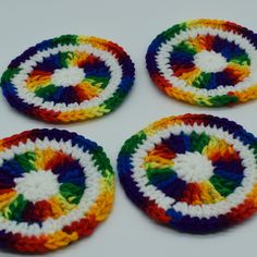 four crocheted coasters are arranged on a white surface with multicolored circles