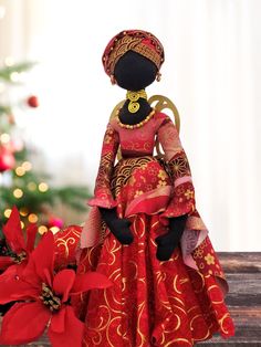 a doll dressed in red and gold sitting on a table next to a christmas tree