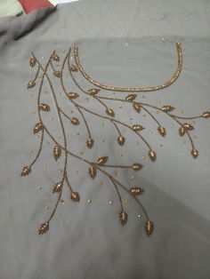 an embroidered fabric with gold beads and leaves on it's side, sitting on top of a bed