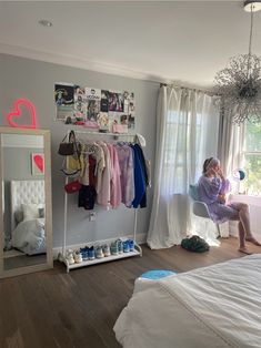 a woman sitting on a chair in front of a window next to a white bed