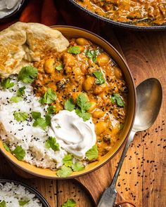 a bowl filled with rice and chicken curry next to pita bread on a wooden table