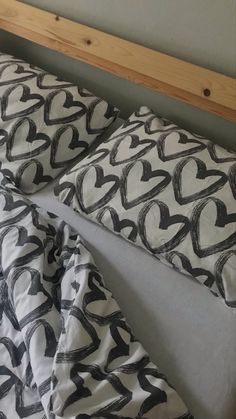 a bed with black and white hearts on the pillow cover, next to a wooden headboard