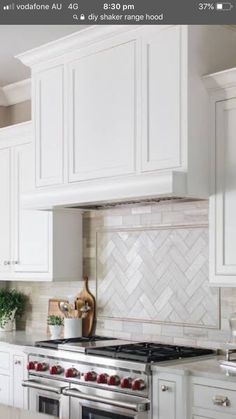 a kitchen with white cabinets and stainless steel stove top oven, range hood, and marble backsplash