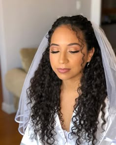 a woman with long hair wearing a veil and looking down at her wedding day makeup