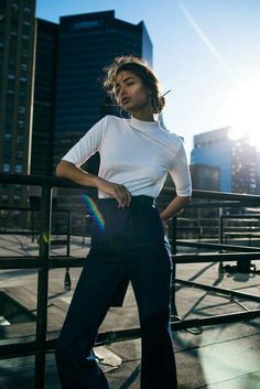 a woman standing on top of a roof next to tall buildings with her hands in her pockets