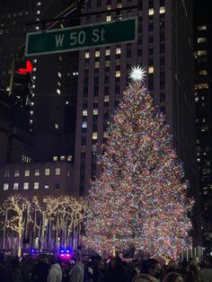 a large christmas tree is lit up in front of the street sign for w 50 st