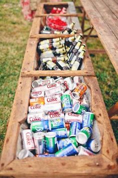 a long wooden table with cans and cans in it on top of green grass next to a picnic table