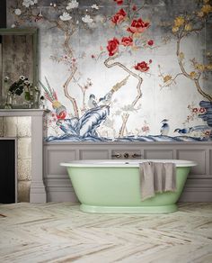 a bath tub sitting in front of a wall with flowers on it and a mirror above it