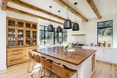 a large kitchen with wooden floors and white walls, along with black pendant lights hanging from the ceiling