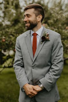 a man in a gray suit and red tie smiles at the camera while standing outside