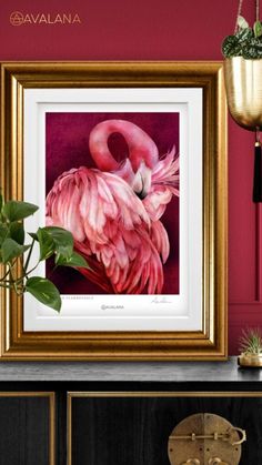 a pink flamingo in a gold frame on a wall next to a potted plant