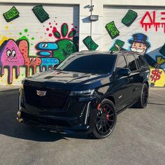 a black suv is parked in front of graffiti covered garage doors and wall with cartoon characters on it