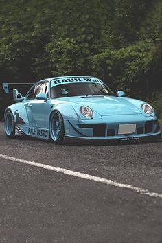 a blue sports car driving down a road next to some trees and bushes in the background