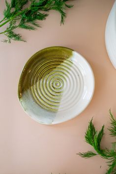 a white and green plate sitting on top of a pink surface next to some plants