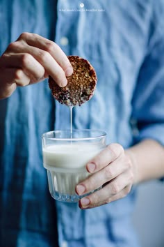 a person is dipping something into a glass with some milk in it and the other hand is holding an oatmeal