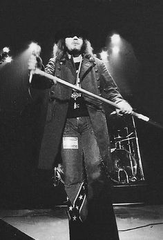 a man with long hair holding a stick in his right hand while standing on stage