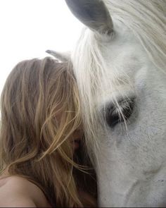 a woman is hugging a white horse with her face close to it's head