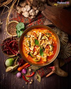 a bowl filled with food on top of a wooden table next to vegetables and spices