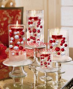 red and white candles sitting on top of a glass table next to vases filled with pearls