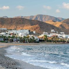 a beach with mountains in the background and houses on the shore near the water's edge