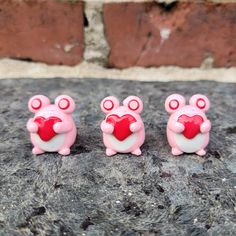 three little pink bears holding a heart on top of a stone slab in front of a brick wall