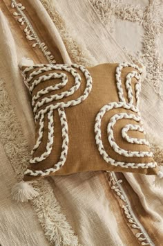 a brown pillow with white braiding on it sitting on top of a beige blanket